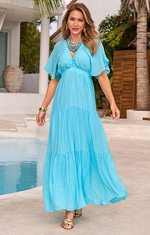 Model is wearing maxi bright blue dress with gold sandals